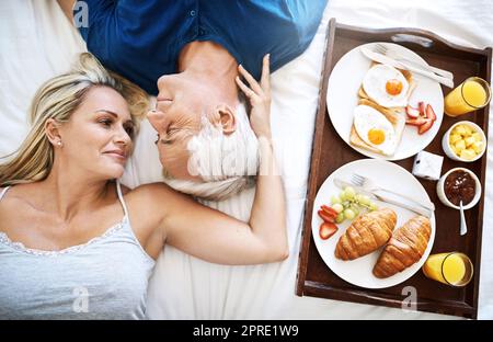 L'amour est rempli des moments les plus doux. Un couple affectueux et mature qui prend son petit déjeuner au lit à la maison. Banque D'Images