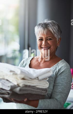 Tout le monde appelle pour des serviettes fraîchement lavées. Portrait d'une femme mûre tenant des serviettes fraîchement pliées tout en faisant la lessive à la maison. Banque D'Images