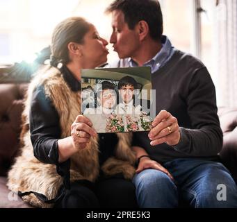 Je vous ai adoré, je vous aime maintenant et pour toujours. Un heureux couple mature tenant une vieille photo de leur mariage à la maison. Banque D'Images