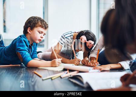 Ils adorent être créatifs. Les enfants se colorent lorsqu'ils sont allongés sur le sol. Banque D'Images