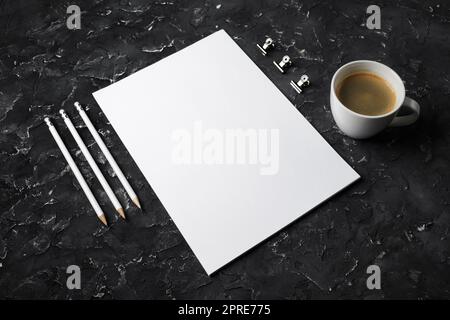 Photo de la papeterie vierge sur fond de plâtre noir. Presse-papiers, papier à en-tête, tasse à café et crayons. Banque D'Images