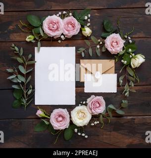 Cartes et enveloppe entre roses roses roses et crème sur bois brun vue de dessus, maquette de mariage. Scène romantique avec cartes et fleurs pastel. Valent Banque D'Images