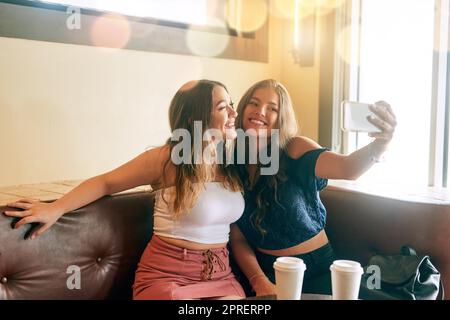 Gimme votre meilleur sourire. Deux jeunes femmes séduisantes prenant des selfies dans leur café local. Banque D'Images