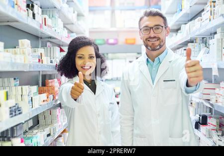 Dites oui à la bonne santé. Portrait d'un homme mature et d'une jeune femme confiants montrant les pouces vers le haut dans une pharmacie. Banque D'Images