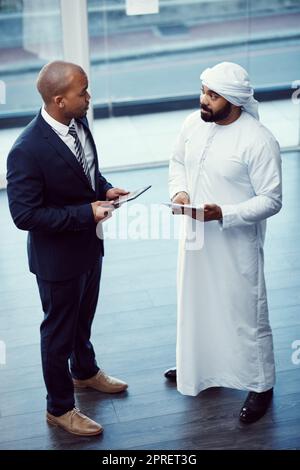 Réunez-vous et faites des choses formidables dans le monde des affaires. Deux hommes d'affaires utilisent des tablettes numériques tout en discutant dans un bureau moderne. Banque D'Images