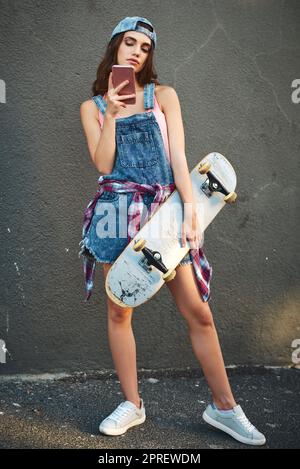 Il est temps de faire du patinage. Portrait d'une jeune femme insouciante tenant un skateboard sur fond gris. Banque D'Images
