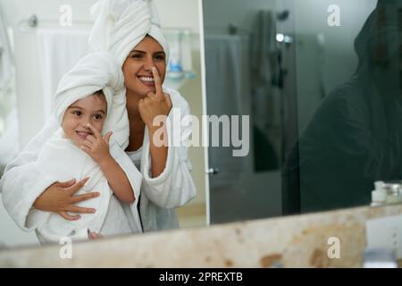 Une mère et une fille hydratant leur visage ensemble dans la salle de bains à la maison. Banque D'Images