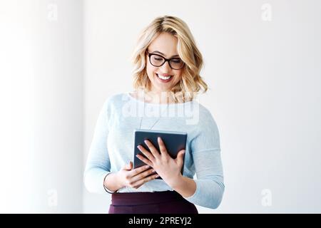 Rester au fait des dernières nouveautés en matière d'affaires. Une jeune femme d'affaires attirante utilisant une tablette numérique dans un bureau. Banque D'Images