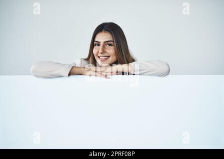 Ai-je quelque chose à partager avec vous... Photo en studio d'une jeune femme d'affaires attirante derrière un écriteau vierge. Banque D'Images