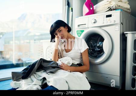 Je préférerais simplement m'asseoir ici et ne rien faire. Une jeune femme attrayante regardant s'ennuyer tout en faisant la lessive à la maison. Banque D'Images