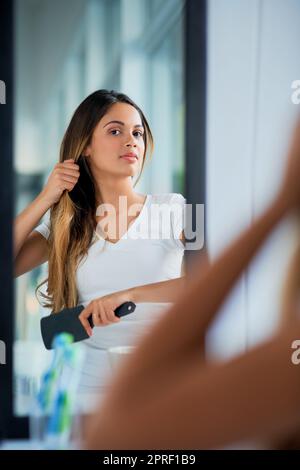 Peignant ses cheveux pour un style doux et élégant. Une jeune femme attrayante se brossant ses cheveux dans la salle de bains. Banque D'Images