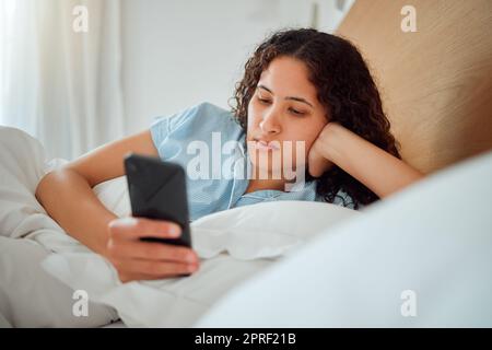 Une jeune femme consulte son téléphone et les réseaux sociaux au lit, navigue sur Internet après être réveillée par SMS à la maison. Femme se détendant, discutant en ligne et streaming. Dame se sentant paresseuse le week-end Banque D'Images
