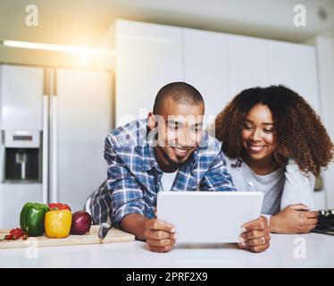 Découvrez différentes recettes en ligne. Un jeune couple utilisant une tablette à la maison. Banque D'Images