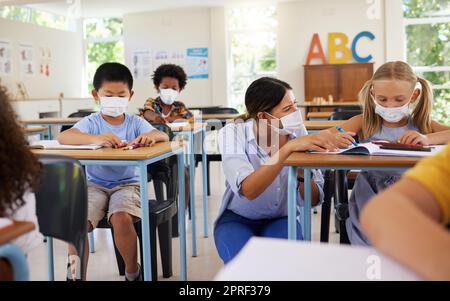 Apprentissage Covid avec des enseignants et des élèves ayant des leçons, des études et de l'éducation en classe pendant une pandémie. Éducateur aidant, montrant et parlant aux jeunes enfants de la maternelle, de la maternelle et de l'élémentaire Banque D'Images