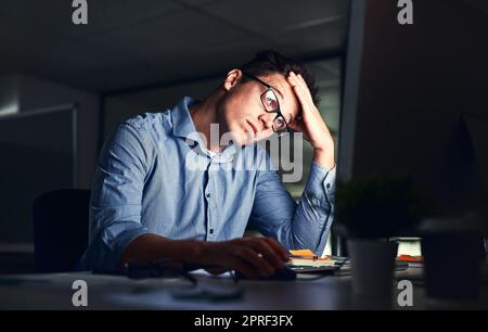 Homme d'affaires fatigué et stressé souffrant de maux de tête, travaillant tard dans la nuit dans le bureau. Sérieux, frustré et surtravaillé homme d'entreprise avec des maux de tête regardant son écran dans le noir. Banque D'Images