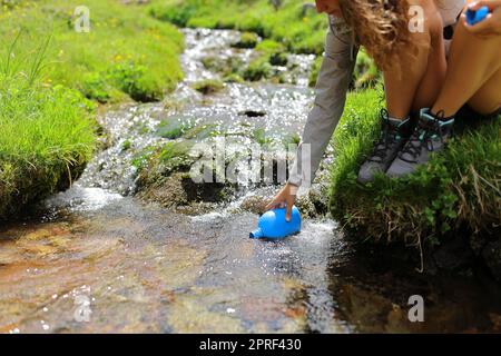 Randonneur à la main remplissant la cantine d'eau brute dans un ruisseau Banque D'Images