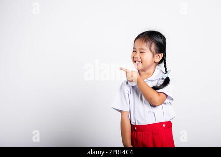 Asiatique tout-petit sourire Happy Wear étudiant thaïlandais uniforme rouge jupe continue de pointer le doigt sur l'espace de copie Banque D'Images