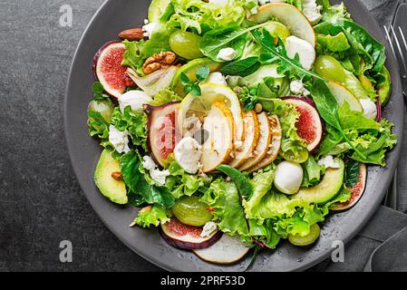 Salade verte fraîche avec fromage mozzarella, fruits et noix sur fond sombre gros plan. Concept pour un repas savoureux et sain Banque D'Images