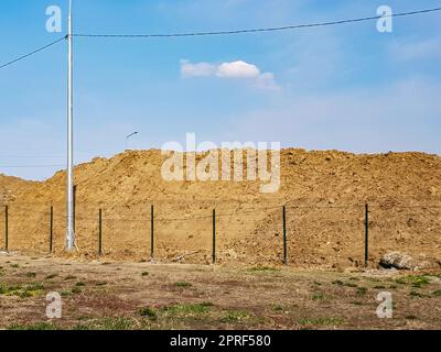 Travaux de terrassement en extérieur avec une grande pile de sable derrière la clôture et un paysage céleste Banque D'Images