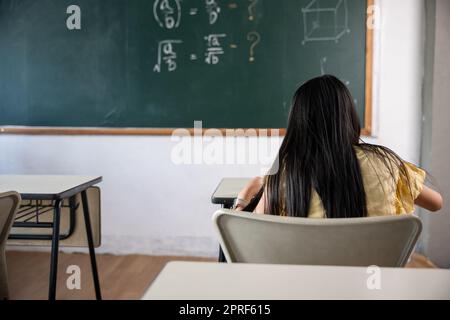 Vue arrière de l'école fille sur la leçon en classe écrire dur sur le tableau noir Banque D'Images