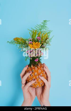 La terre rit en fleurs. Une femme méconnaissable tenant un ananas farci de fleurs. Banque D'Images