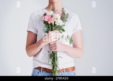 Je veux me sentir libre comme les fleurs. Photo de studio d'une femme méconnaissable portant un bouquet de fleurs sur fond gris. Banque D'Images