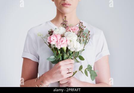 Les fleurs sont des natures cadeaux pour le coeur. Photo en studio d'une femme méconnaissable portant un bouquet de fleurs sur un fond gris. Banque D'Images