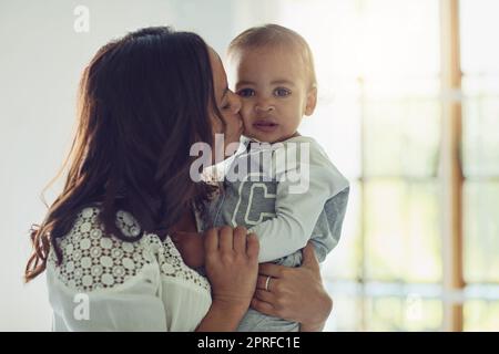 Juste un peu plus de baisers avant vous pas peu plus. Une mère embrassant son adorable bébé garçon sur la joue à la maison. Banque D'Images