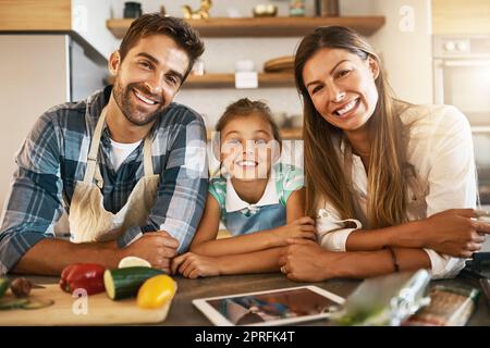 L'amour de la nourriture est dans cette famille. Portrait de deux parents heureux et de leur jeune fille essayant ensemble une nouvelle recette dans la cuisine. Banque D'Images