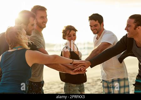 Ils se tiennent entourés de positivité. Un groupe de jeunes amis heureux mettant leurs mains dans un tas sur la plage. Banque D'Images