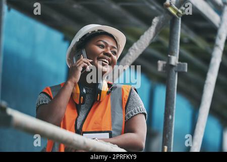 Le directeur de la construction, l'entrepreneur et l'ingénieur parlent au téléphone tout en planifiant la logistique sur un chantier de construction en ville. Jeune femme architecte, superviseur et urbaniste heureuse, souriante et gaie Banque D'Images