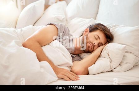 Détendez-vous, dormez et la tranquillité d'un homme fatigué dormant dans un lit à la maison. Rêvant, relaxant et reposant calme personne attrayante avec les yeux fermés sur un oreiller à sa maison le matin prenant une sieste Banque D'Images