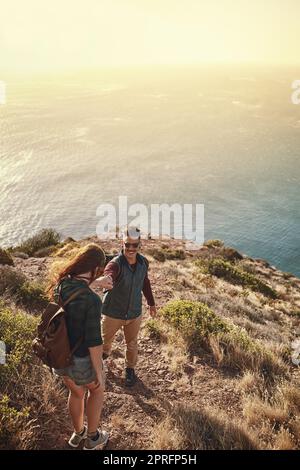 Laissez-moi vous donner une main. Photo en grand angle d'un jeune homme qui aide sa petite amie alors qu'ils font de la randonnée dans les montagnes. Banque D'Images