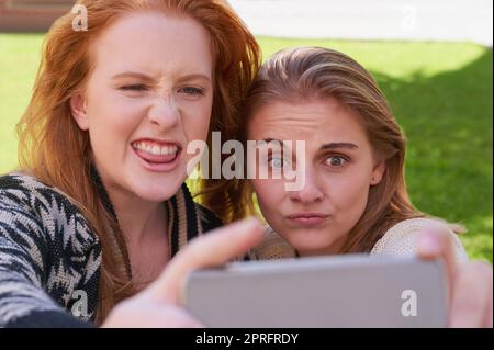 Les meilleurs amis sont des gens qui sont votre genre de fou. Deux jeunes amis prenant un selfie avec un téléphone. Banque D'Images