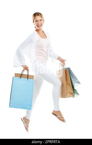 Lorsqu'une vente appelle, je suis en train de courir. Portrait studio d'une jeune femme heureuse portant des sacs à provisions et sautant sur fond blanc. Banque D'Images