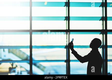 Il y a tellement de choses à voir à l'aéroport. Un voyageur non identifiable utilisant son smartphone dans un salon d'aéroport vide. Banque D'Images