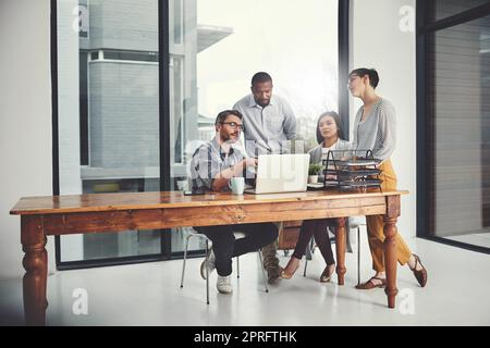 Le travail d'équipe fait le travail de rêve. Photo d'un groupe d'hommes d'affaires rassemblés autour d'un ordinateur portable dans leur bureau. Banque D'Images