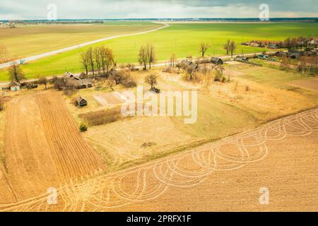 Bélarus. Vue aérienne du village bélarussien. Magnifique paysage rural avec vue panoramique. Début de la saison agricole du printemps. Chenilles sur champ labouré de machines agricoles Banque D'Images