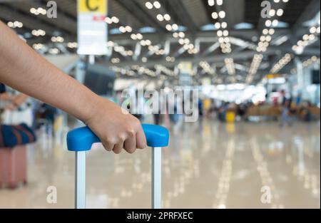 Femme tenant la poignée à bagages avec un arrière-plan flou du terminal de l'aéroport. Banque D'Images