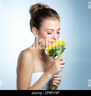 Shes une beauté délicate. Photo studio d'une belle jeune femme qui sent un tournesol. Banque D'Images