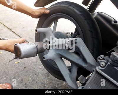 Gros plan d'un mécanicien de moto utilisant un pistolet pneumatique pour desserrer les écrous de roue dans un atelier mécanique Banque D'Images