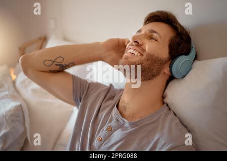 Homme écoutant de la musique, des podcasts ou de la radio avec un casque à la maison tout en se relaxant, sourire et heureux dans sa chambre. Paisible, libre et jeune homme en streaming une liste de lecture audio en ligne en appréciant le week-end Banque D'Images