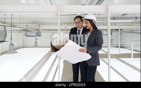 Ingénieur en casque de sécurité tenir le plan de construction du système de ventilation tout en faisant vérifier la propreté de l'usine par l'inspecteur du bâtiment. panneaux d'éclairage et de climatisation montés au plafond. Banque D'Images