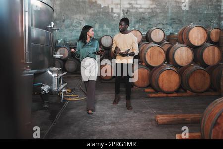 Un employé de cave à vin, d'entrepôt et de cave de vinification enseigne à un homme le vin pendant qu'il écrit des notes. Viticulteur marchant dans une distillerie avec des barils en bois et des machines agricoles tout en consultant un partenaire Banque D'Images