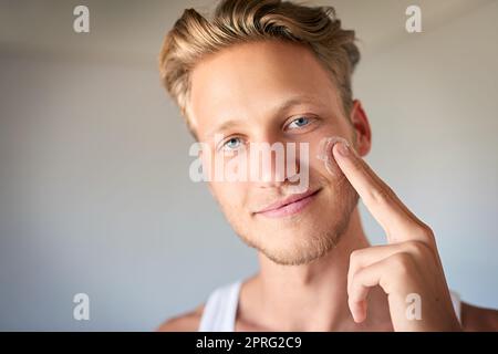 Gardez la peau hydratée et protégée. Un jeune homme appliquant une crème hydratante sur son visage. Banque D'Images