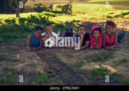 Footballeurs en préparation. Un groupe d'enfants allongé avec un ballon de football sur un peu d'herbe dehors. Banque D'Images