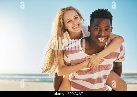 Rien ne dit de romance estivale comme une promenade en pigeyback. Un jeune couple heureux qui profite d'une promenade en pigeyback à la plage. Banque D'Images