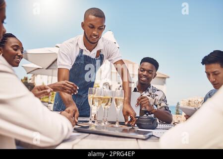 Restaurant sur la plage, serveur et célébration au champagne avec des amis. Hospitalité, cuisine fine et un repas en plein air relaxant avec les gens. Vacances d'été ou pause déjeuner dehors avec vue sur l'océan. Banque D'Images