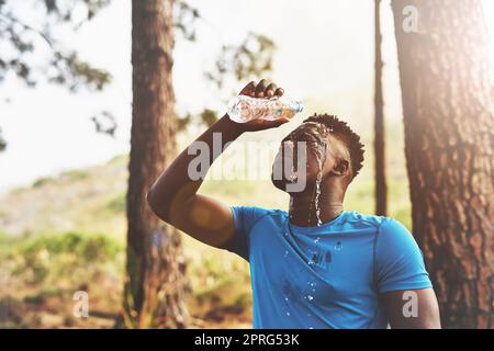 Après un entraînement intense, un jeune sportif qui coule de l'eau sur son visage pendant une course dans la forêt. Banque D'Images