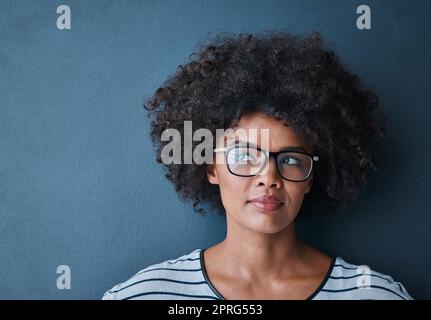 Le début d'une idée brillante. Photo en studio d'une jeune femme attrayante portant des lunettes et regardant réfléchie sur fond bleu. Banque D'Images
